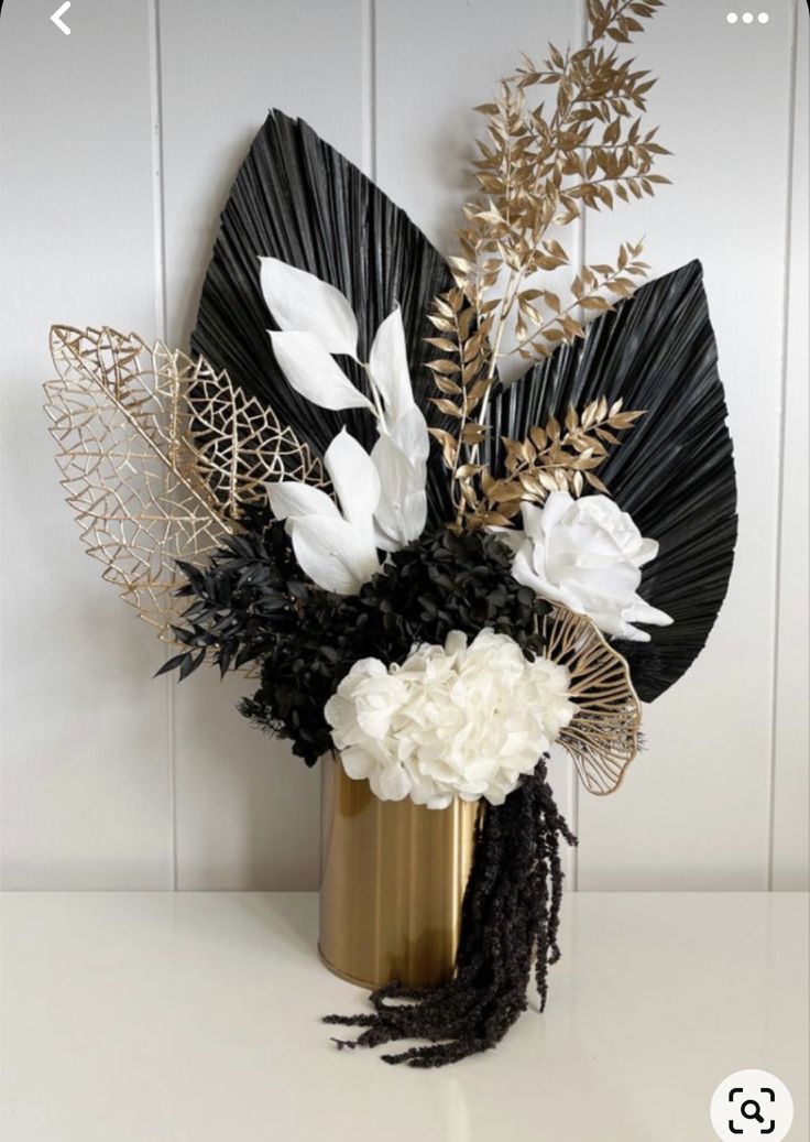 a vase filled with flowers and leaves on top of a white table next to a wall