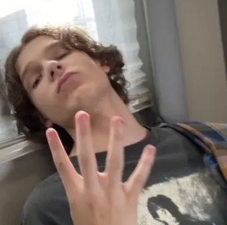 a young man making the vulcan sign with his hand while sitting in front of a window