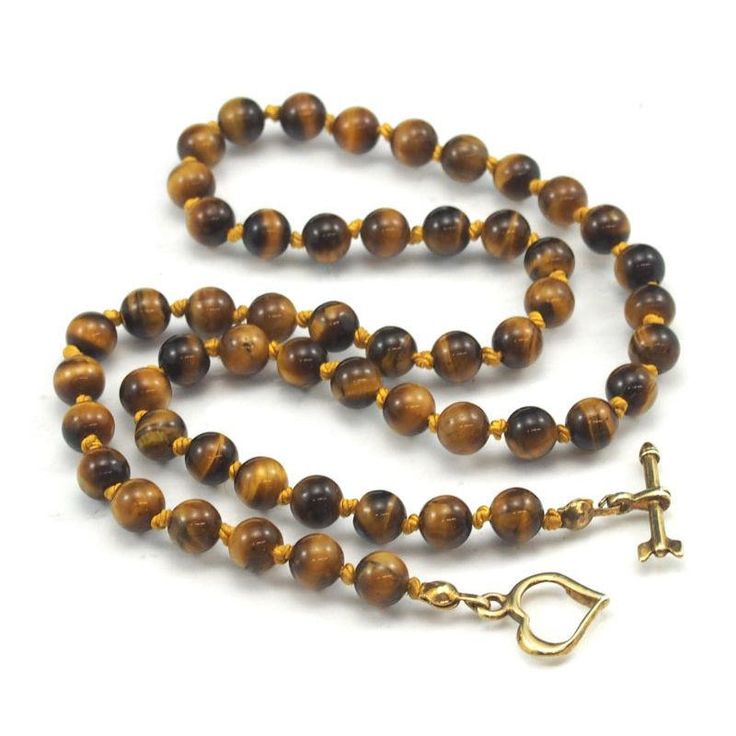 Tiger's Eye Necklace with Gold Plated Toggle Clasp Approx. 18 1/2" long Bead Size : 6mm Strung and knotted on silk cord Handcrafted at Beads of Paradise NYC Tiger’s Eye is a form of Chalcedony quartz, but is what is a known in mineralogy as a pseudomorph. The term comes from the Greek for "false form." Pseudomorphs form when one mineral replaces another. It began as the fibrous blue mineral called Crocidolite, which is made up of iron and sodium. The Crocidolite was gradually transformed into wh Adjustable Single Strand Lariat Necklace With Round Beads, Gold Jewelry With Hand-knotted Round Beads, Toggle Clasp Necklace With Round Beads, Gold Beaded Necklace With Toggle Clasp, Gold Hand-knotted Necklace For Gift, Gold Hand Knotted Necklace For Gift, Adjustable Brown Hand Knotted Necklaces, Brown Adjustable Hand Knotted Necklace, Adjustable Lariat Necklace With Gemstone Beads