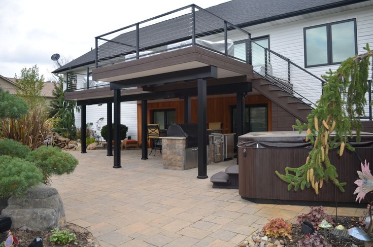 an outdoor hot tub and grill area in front of a house with stairs leading up to it