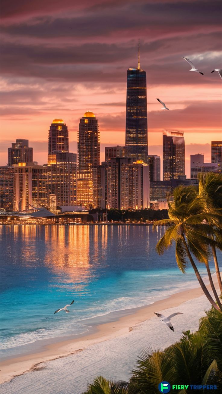 the city skyline is lit up at night as birds fly over the water and beach