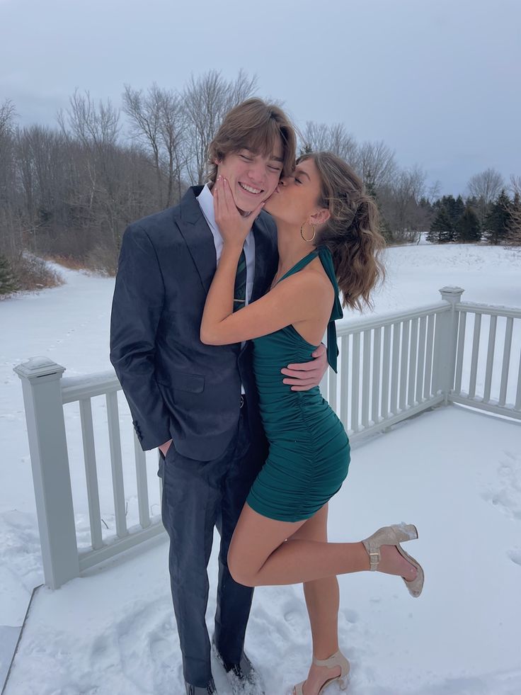 a man in a suit and tie is kissing a woman on the snow covered ground