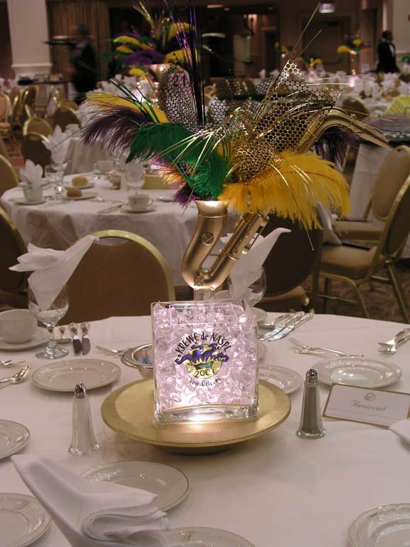 a table set up for an event with white linens and gold plates, silverware, and colorful centerpieces