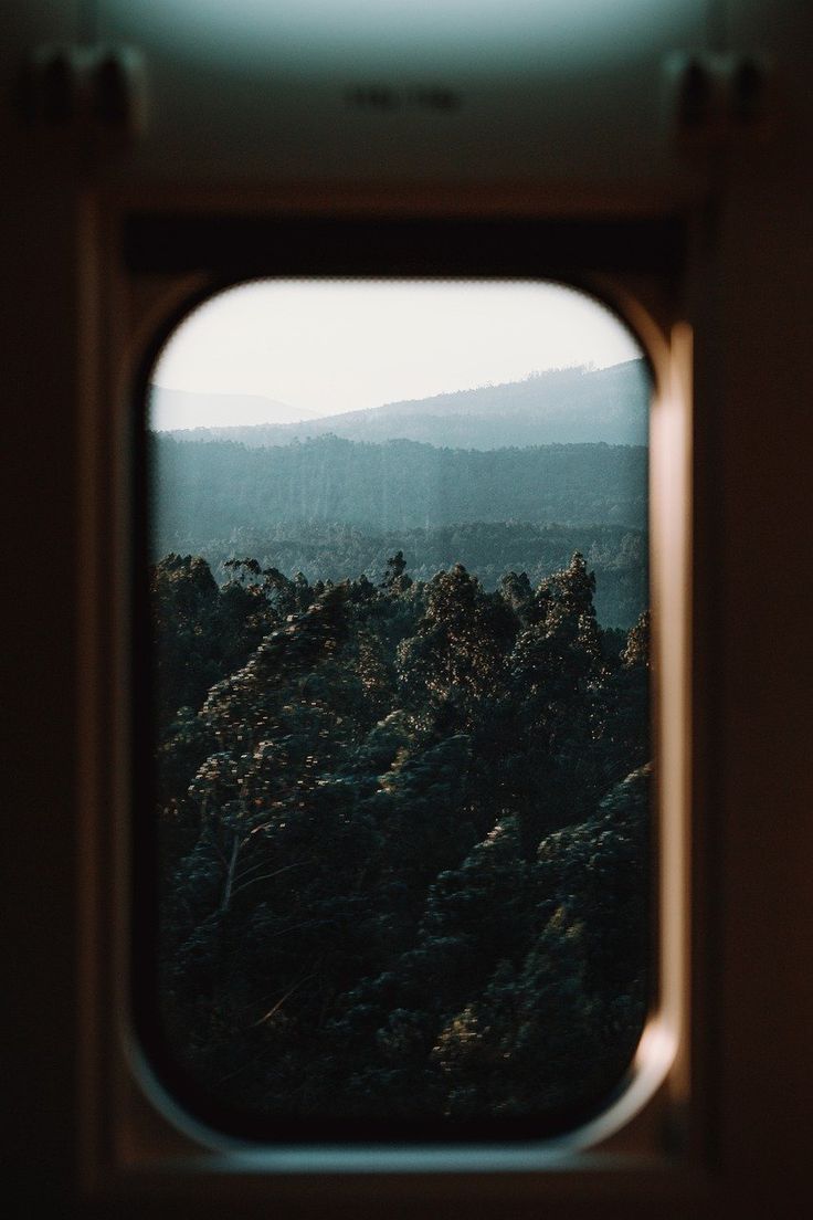 a view out the window of a train looking at trees and mountains in the distance