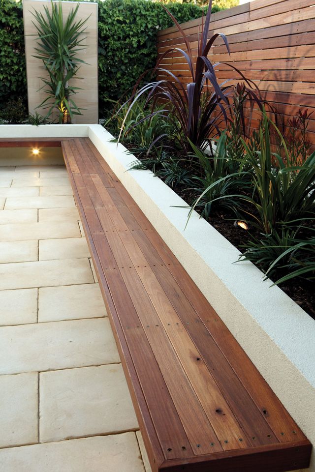 a wooden bench sitting in the middle of a garden next to a wall with plants