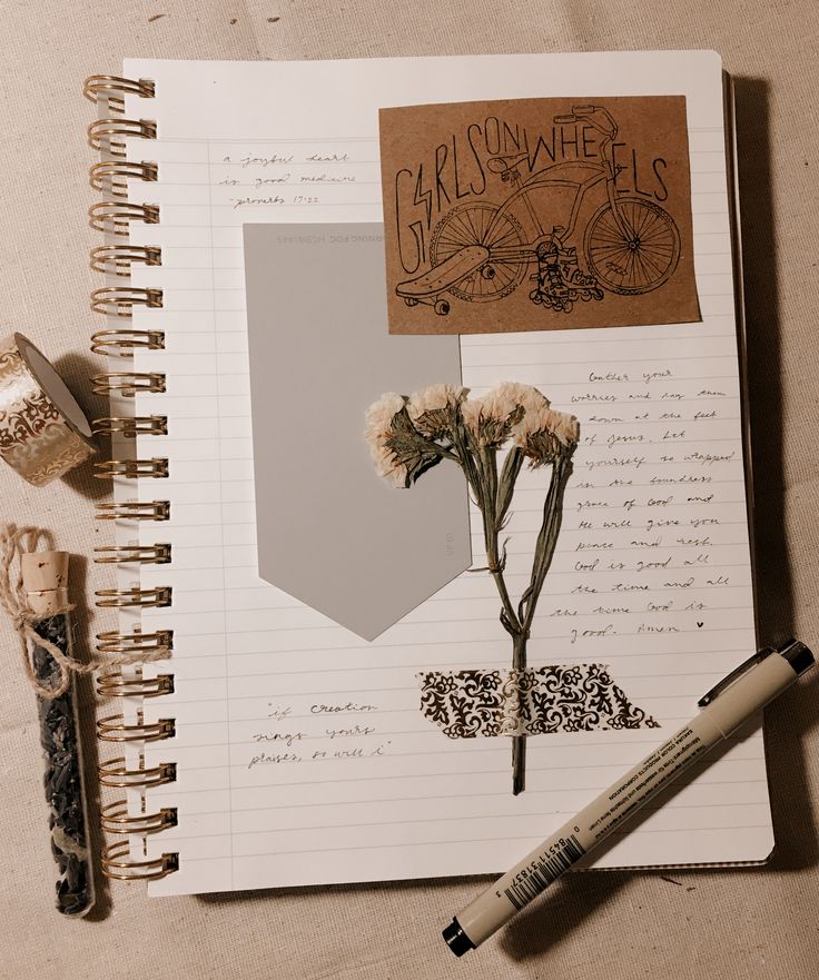 an open notebook with flowers and writing on it next to a pen, paper clippings and other items