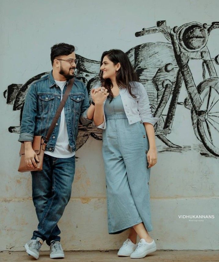 a man and woman standing next to each other in front of a wall with a bicycle painted on it