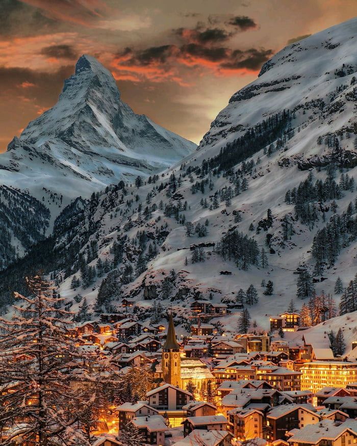 a snowy mountain town at night with lights on the buildings and mountains in the background