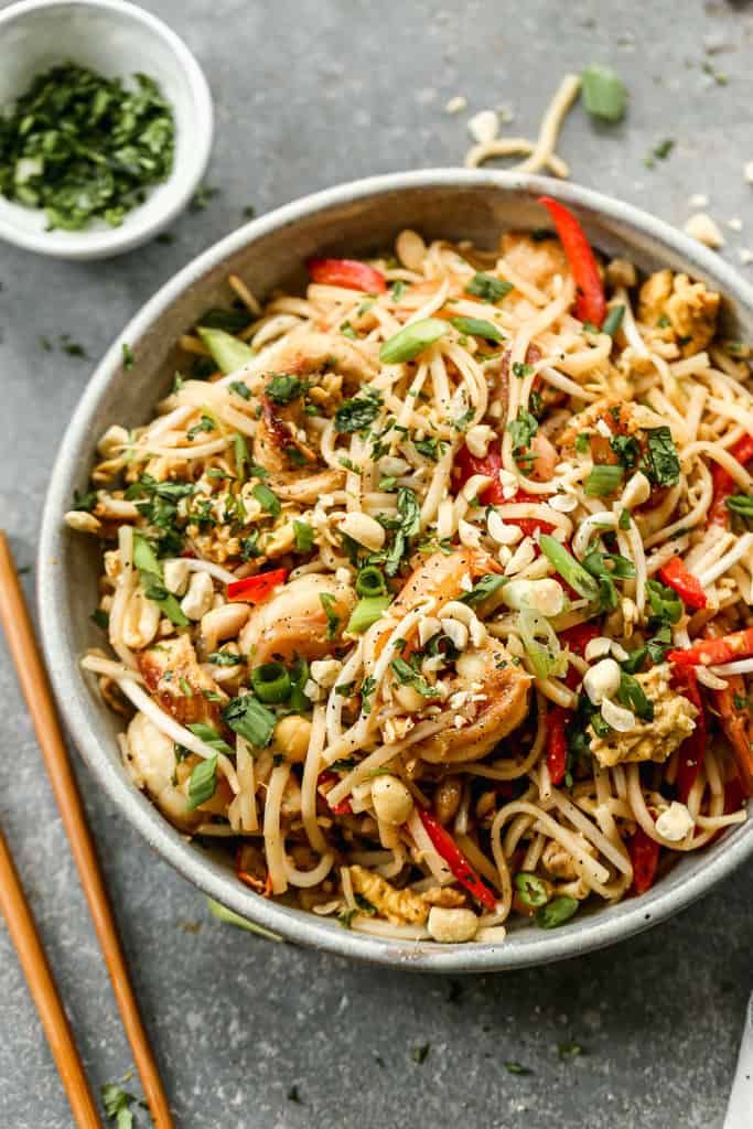 a bowl filled with noodles and vegetables next to chopsticks on a table top