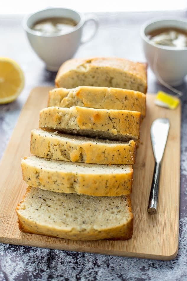 sliced loaf of lemon poppy seed bread on a cutting board with two cups of coffee in the background