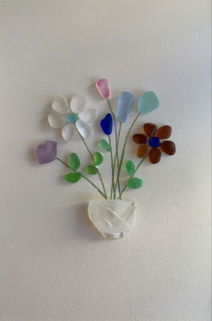 a vase filled with lots of different colored glass flowers on top of a white wall