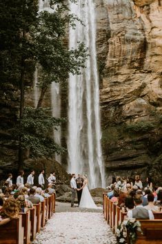 a bride and groom are standing in front of a waterfall at their wedding ceremony with guests seated on pews