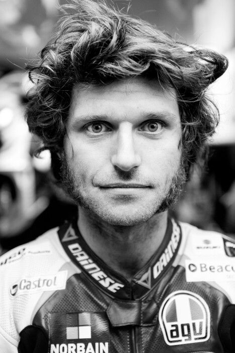 a black and white photo of a man with curly hair wearing a racing suit, looking at the camera