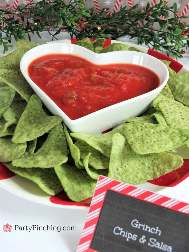 a heart shaped bowl filled with salsa on top of tortilla chips next to a sign