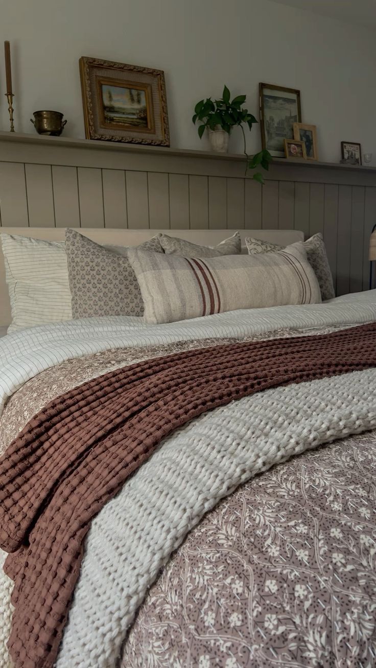 a bed with pillows and blankets on top of it next to a shelf filled with pictures