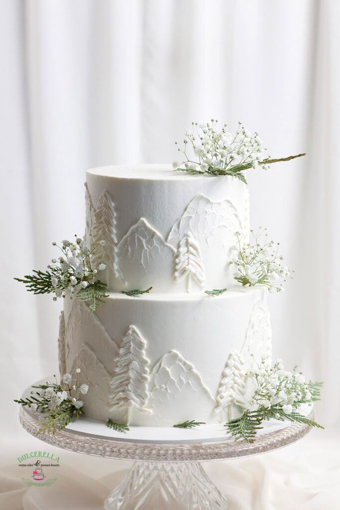 a three tiered white wedding cake with pine trees on top