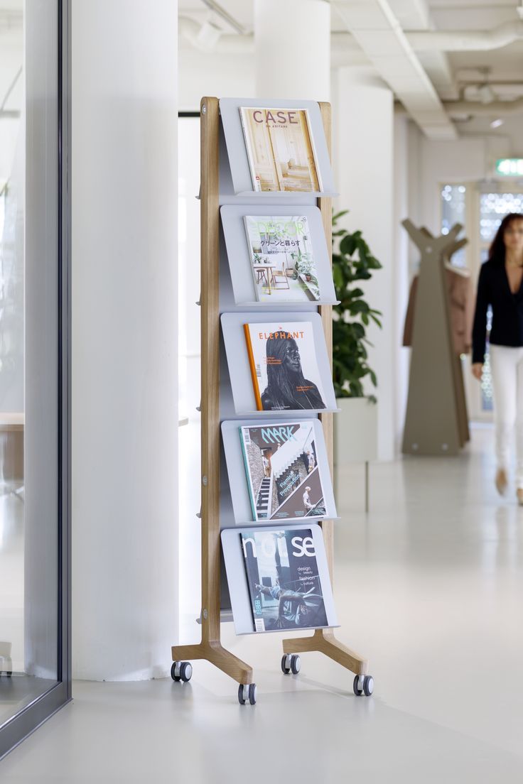 a woman walking through an office building past a tall book rack with pictures on it