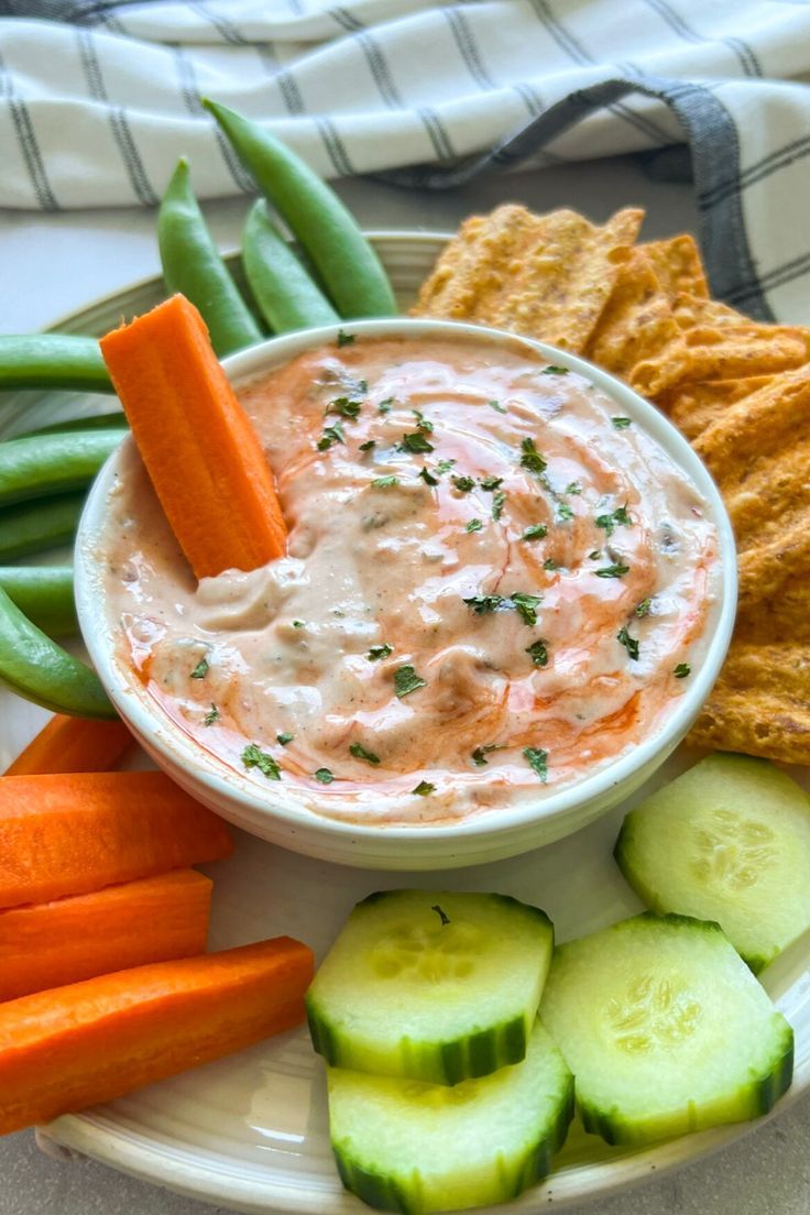 a white plate topped with cucumber, carrots and dip next to crackers