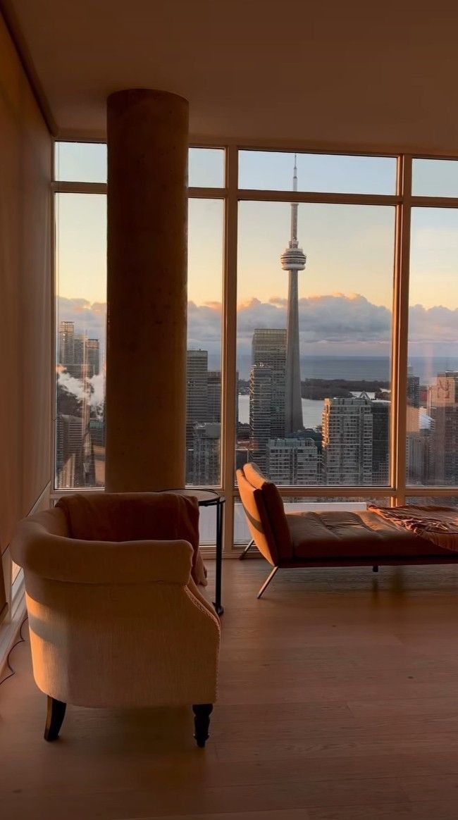 a living room filled with furniture and large windows overlooking the cityscape at sunset