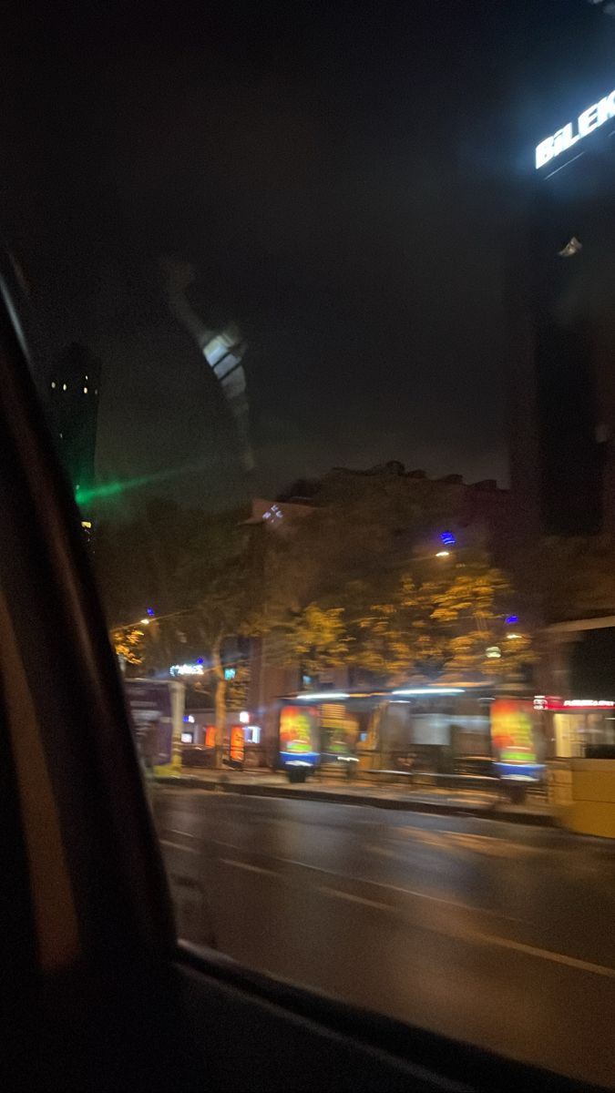 the view from inside a car at night with buildings in the background and lights on