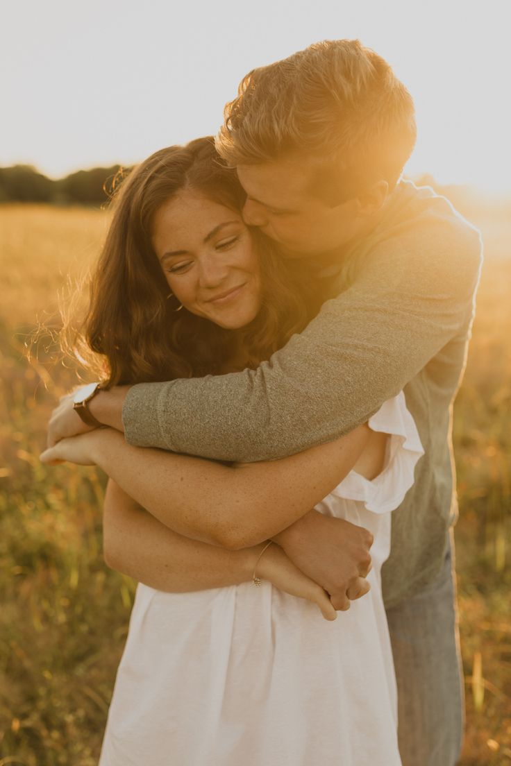 a man and woman hugging in the middle of a field at sunset with the sun shining on them