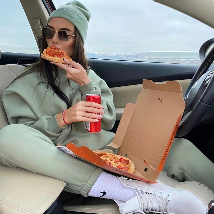 a woman sitting in the back seat of a car while eating pizza and drinking soda