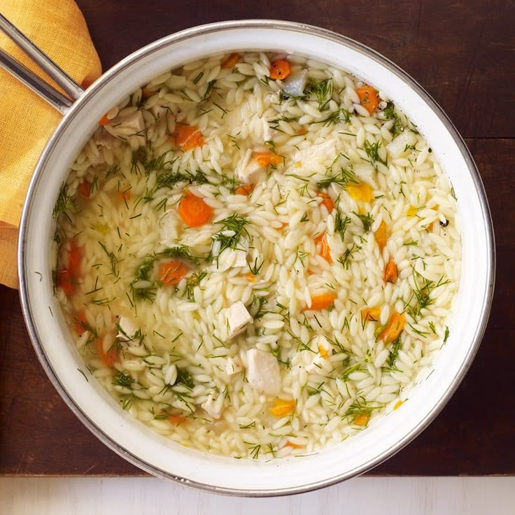 a pot filled with rice and vegetables on top of a wooden table next to a spoon