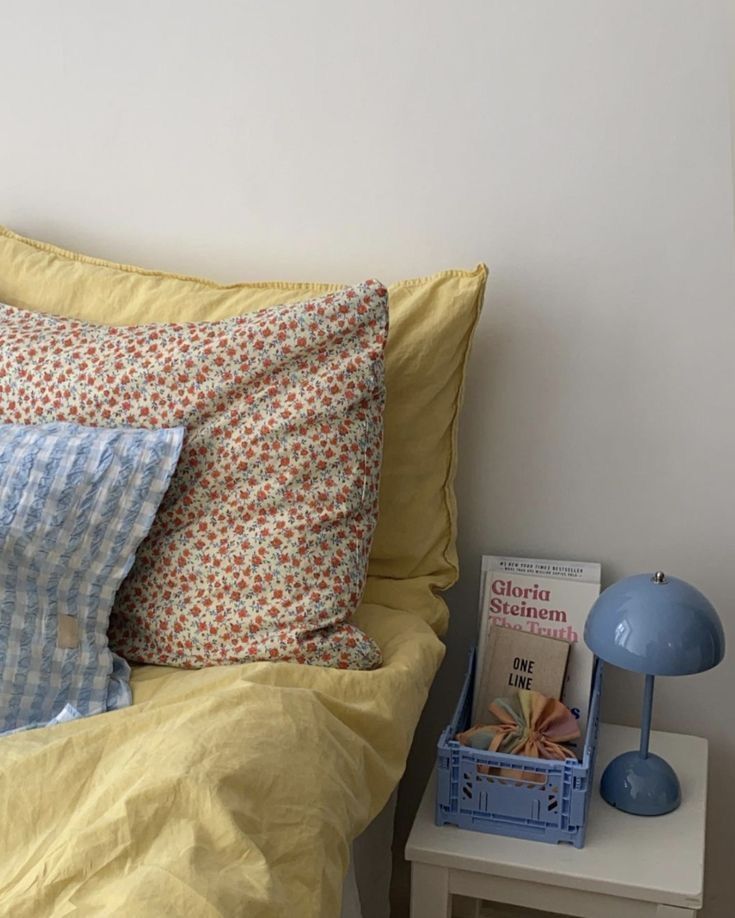 a bed with yellow sheets and pillows next to a blue lamp on a white night stand