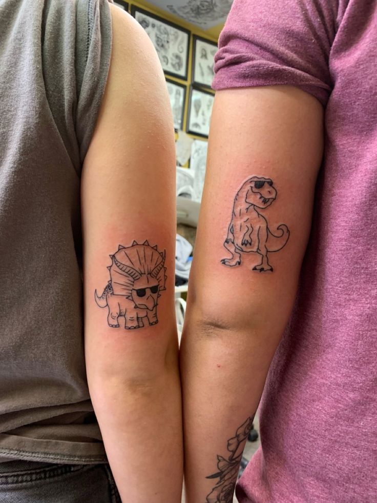 two people with tattoos on their arms, one has a dinosaur and the other has a fish