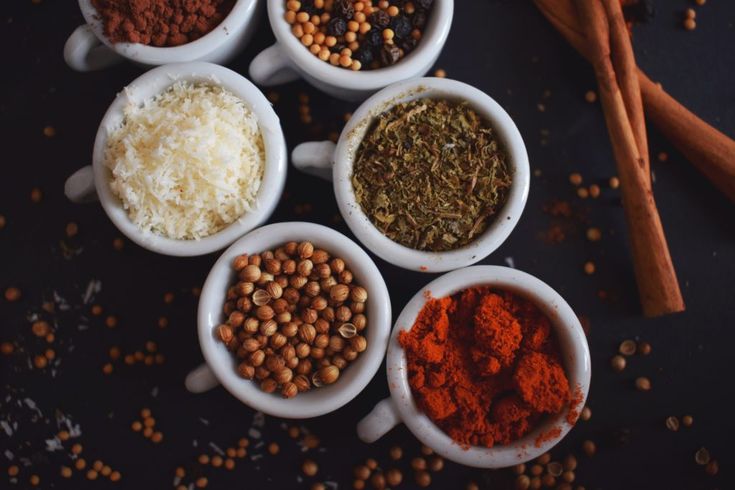 five bowls filled with different spices on top of a black table next to cinnamon sticks