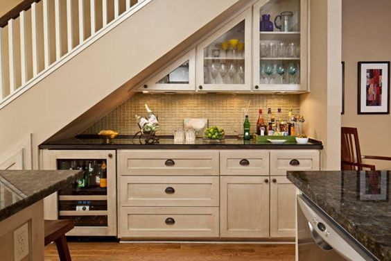 a kitchen with white cabinets and black counter tops under a stair case in an upstairs space