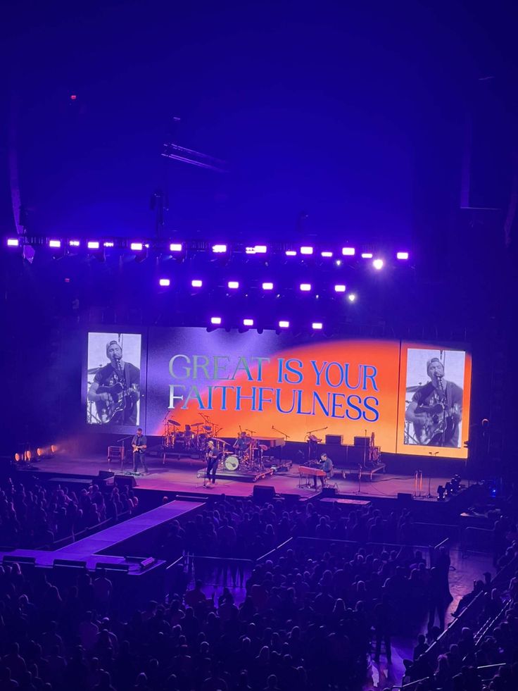 the stage is lit up with purple lights and people are seated on it, watching