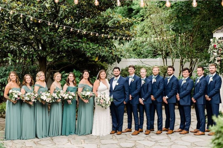 a group of people standing next to each other in front of trees and bushes at a wedding