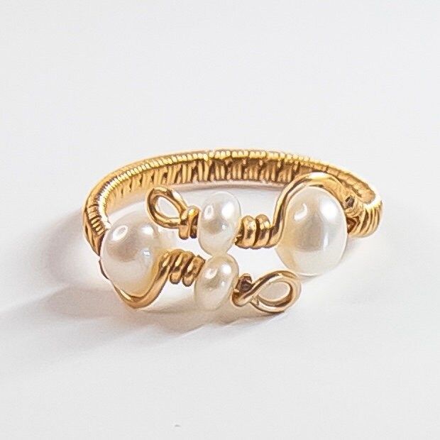 The ring features natural pearls that are carefully wire-wrapped in a unique and intricate design, creating a one-of-a-kind piece. The adjustable band ensures a perfect fit for any finger, making it a versatile addition to any jewelry collection. The combination of natural pearls and handmade wire wrapping makes this ring a truly unique and special piece that will be treasured for years to come. Perfect for any occasion, this pearl ring is an excellent choice for those who appreciate the beauty of natural materials and the artistry of handmade jewelry. MATERIALS: 4 Natural Freshwater Pearls  14K gold plated Jewelry wire MY PROCESS: Inspired by the raw elegance of natural pearls and stones, I handcraft every piece to make them unique and special. This means that each piece is one-of-a-kind Handmade Adjustable Open Pearl Ring, Handmade Dainty Pearl Open Ring, Dainty Handmade Pearl Open Ring, Handmade Pearl Ring As A Gift, Handmade Open Pearl Ring, Dainty Handmade Adjustable Pearl Ring, Adjustable Pearl Drop Ring, Handmade Adjustable White Pearl Ring, Delicate Wire Wrapped Ring Jewelry