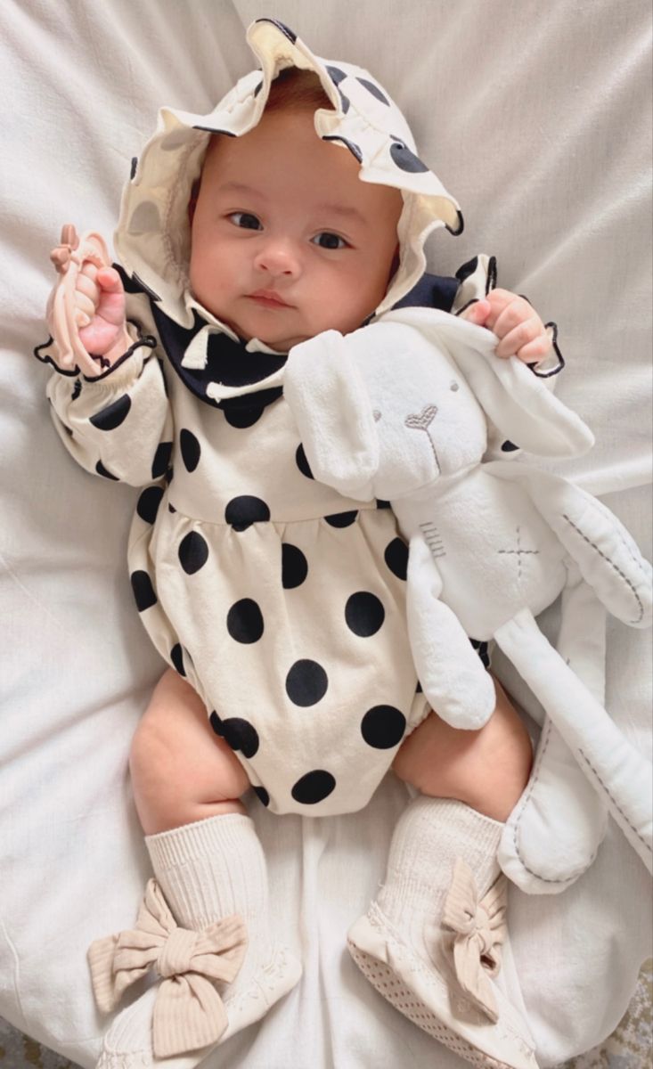 a baby in a polka dot outfit laying on top of a white blanket holding a stuffed animal