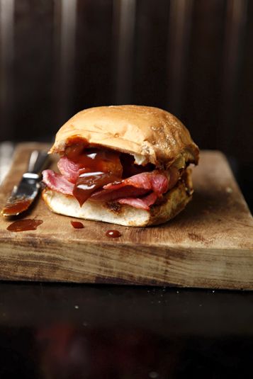 a sandwich sitting on top of a wooden cutting board next to a knife and fork