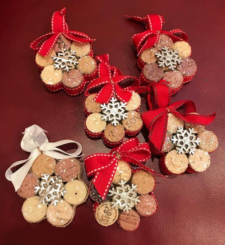 four wine cork ornaments with red bows and snowflakes on them, sitting on a leather surface