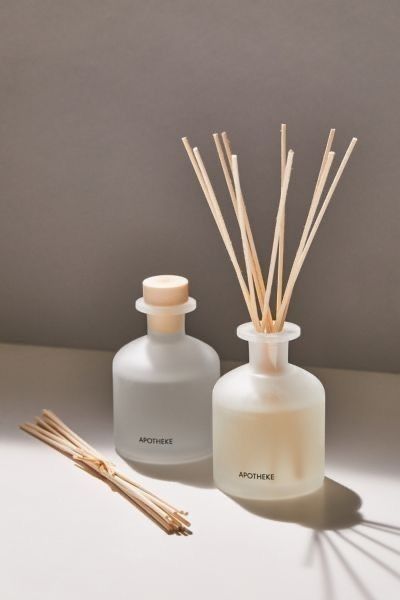 two bottles with reeds next to each other on a white surface, one is empty and the other has sticks in it