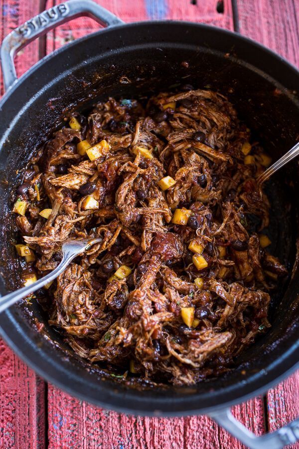 a pot full of shredded meat and vegetables on a wooden table with a spoon in it