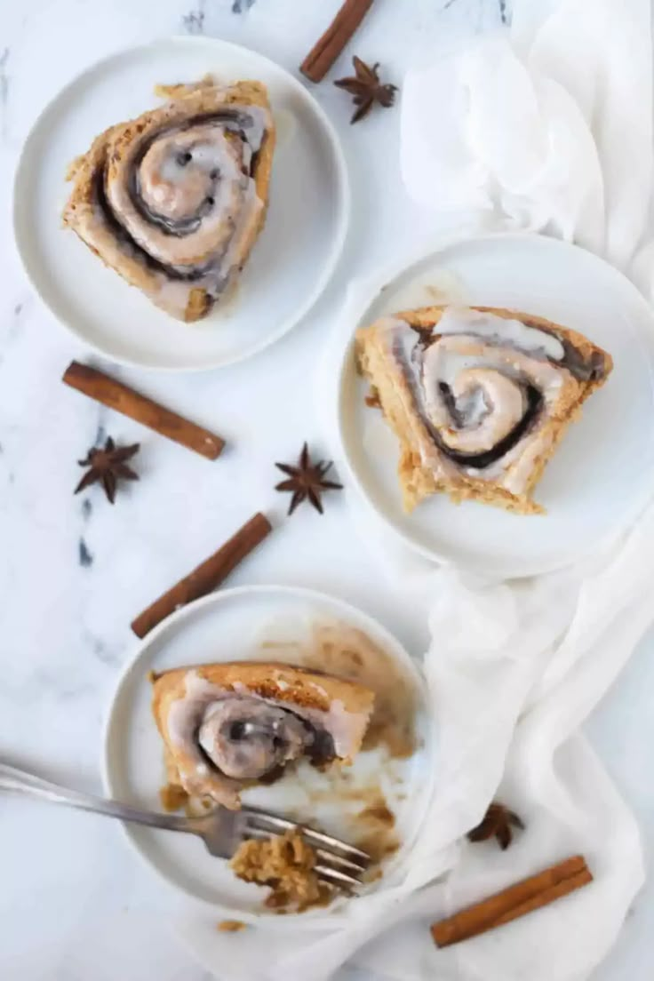 three plates filled with cinnamon rolls on top of a white tablecloth next to cinnamon sticks