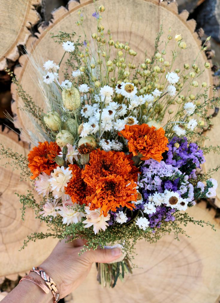 a bouquet of flowers sitting on top of a tree stump next to a person's hand