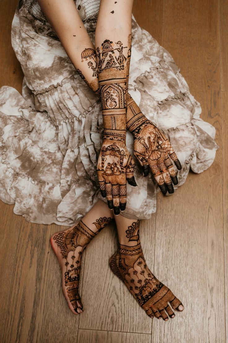 the legs and hands of a woman with henna tattoos on them, sitting on a wooden floor