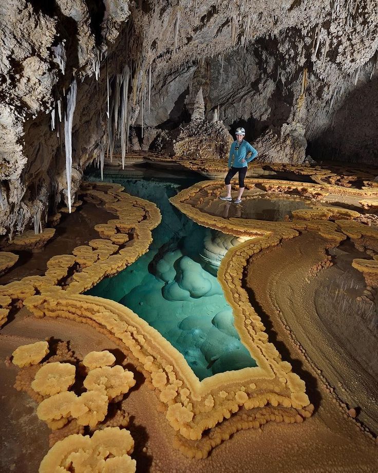 a man standing in the middle of a cave filled with blue water and ice formations