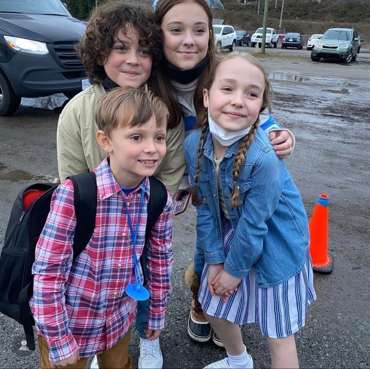 three girls and one boy are standing in the parking lot with their arms around each other