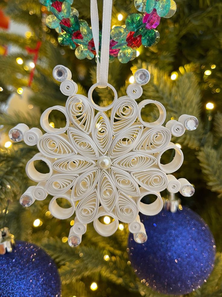 a white snowflake ornament hanging from a christmas tree with ornaments around it