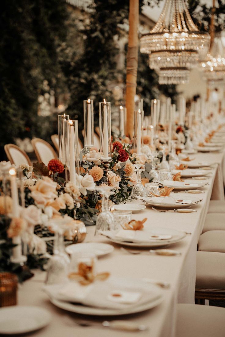 a long table is set with white plates and candles