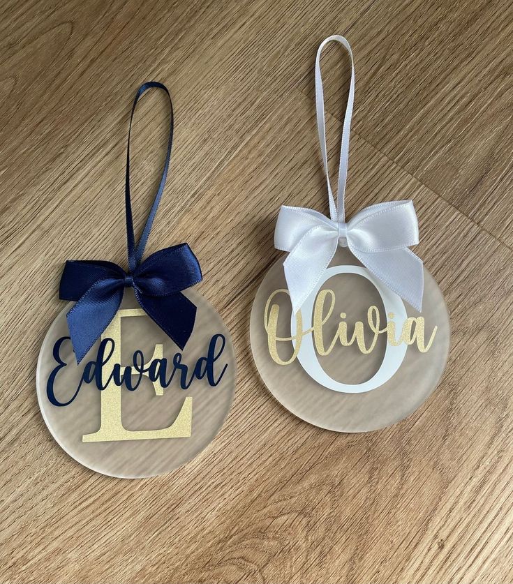 two personalized christmas ornament hanging on a wooden table with ribbon and bow