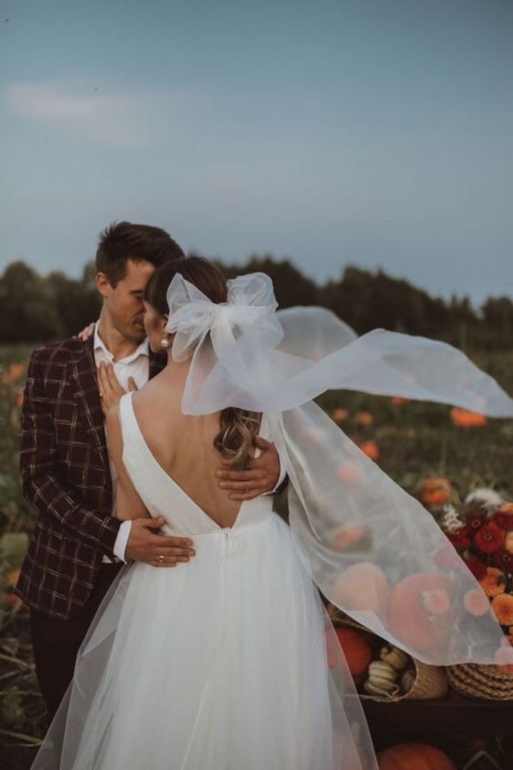 a bride and groom standing in the middle of a field with pumpkins behind them