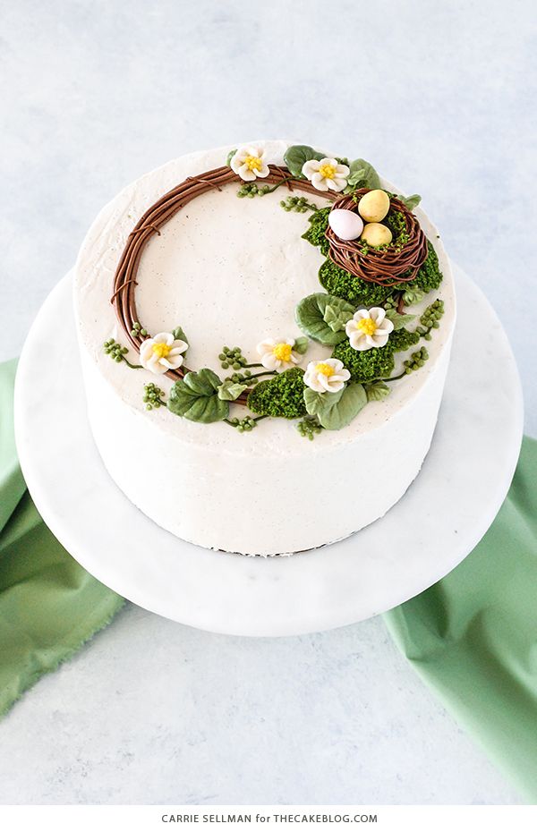 a cake decorated with flowers and birds nest on top of a white platter next to green napkins