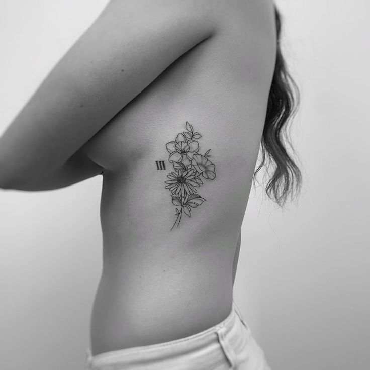 the back of a woman's shoulder with flowers tattooed on her left side ribcage